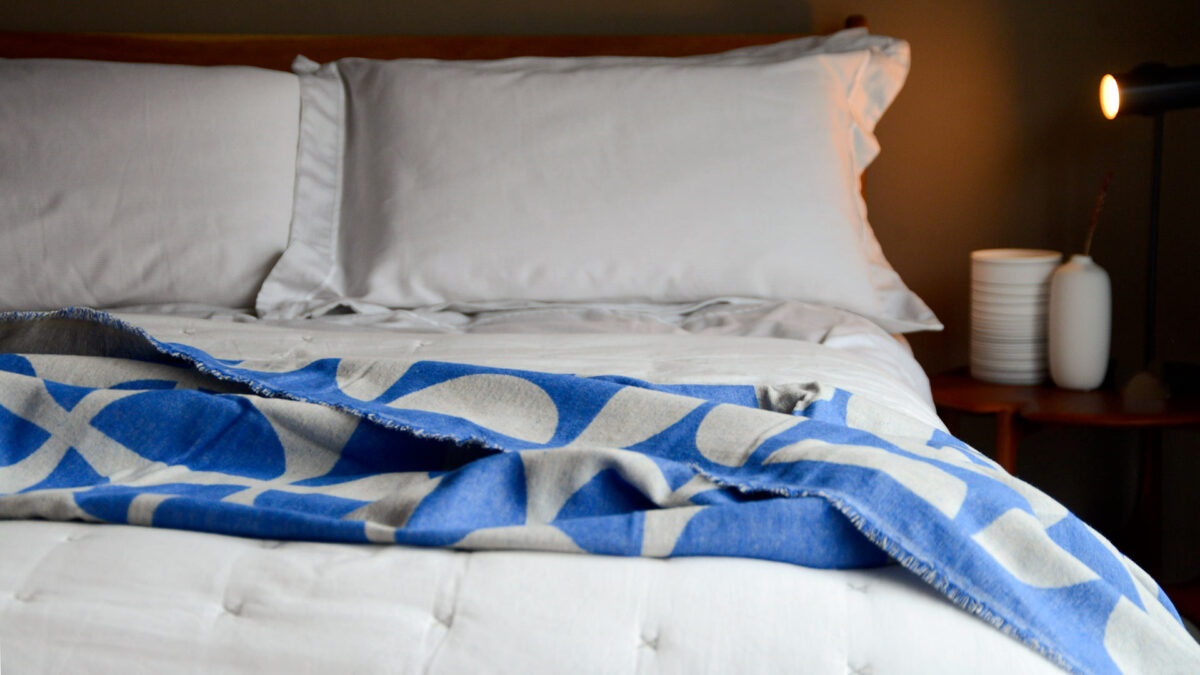 graphic patterned soft cotton throw in blue and ecru shown on a bed