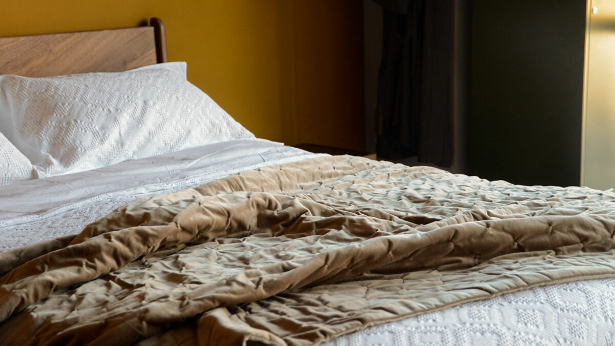 pale brown velvet softly quilted reversible throw shown draped on a kingsize bed