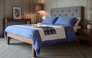 skye a wooden bed with upholstered headboard shown with blue linen bedding